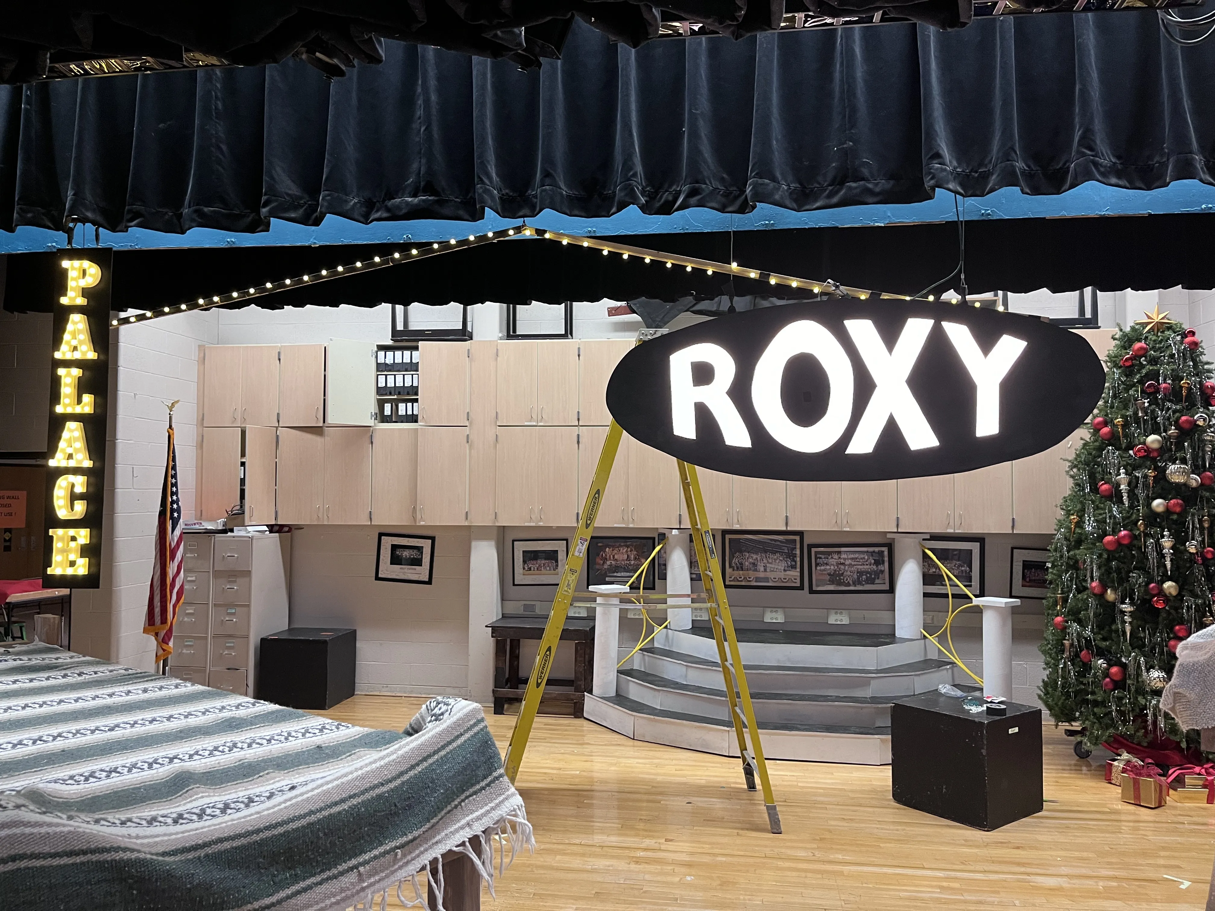 All three NYC signs on stage during setup, with the Warbucks platform visible in the background