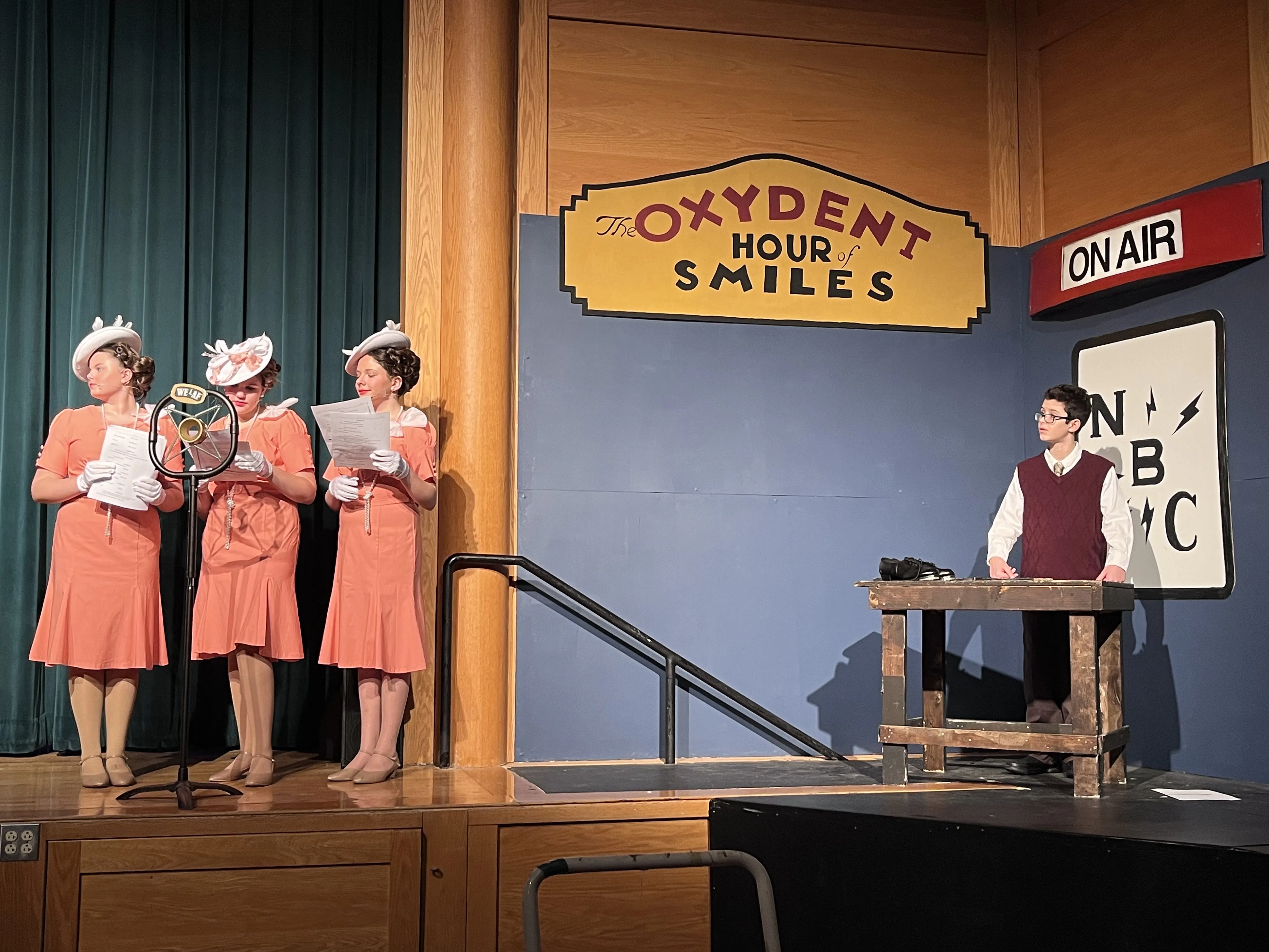 The radio studio scene with actors — the Oxydent sign, ON AIR, and NBC sign all visible