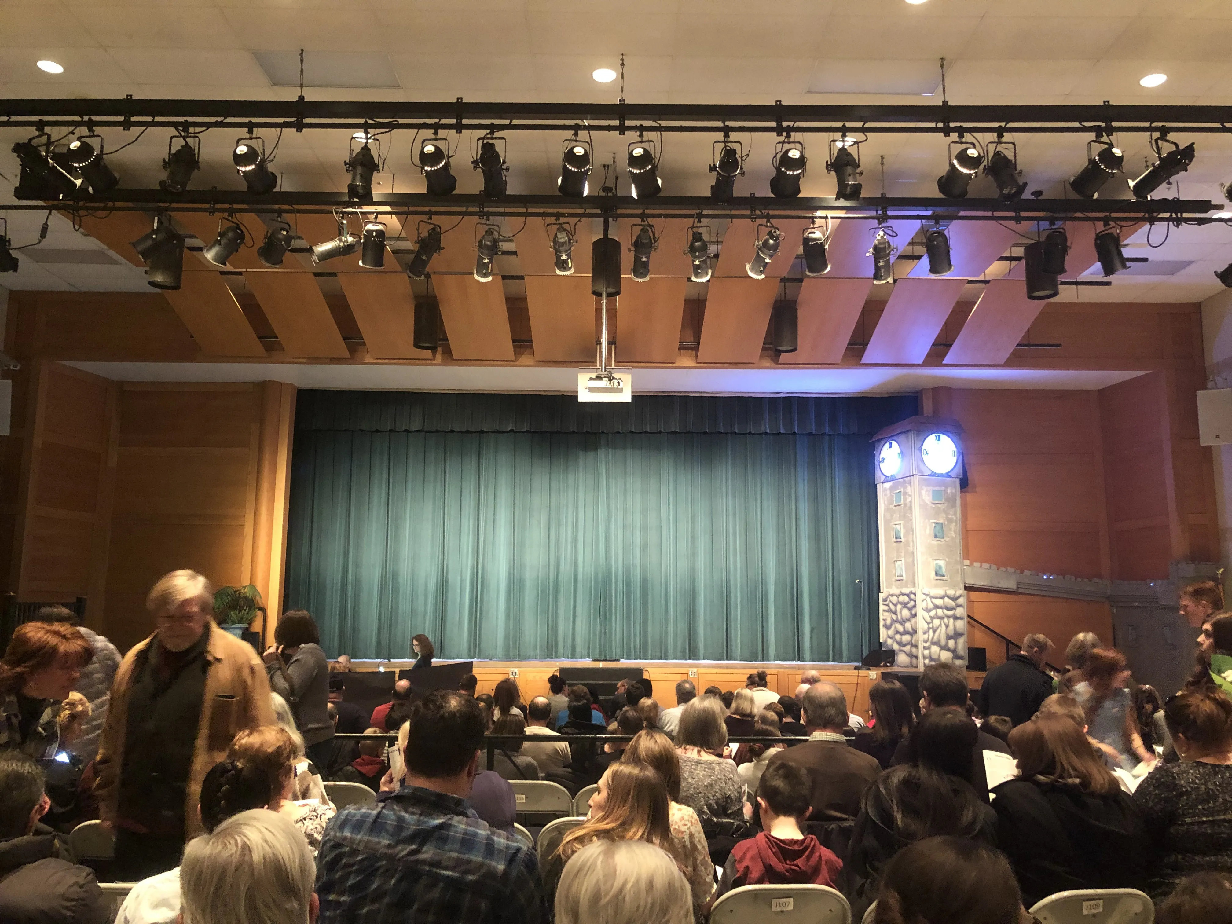 The audience arriving — the clock tower already glowing at the right of the stage