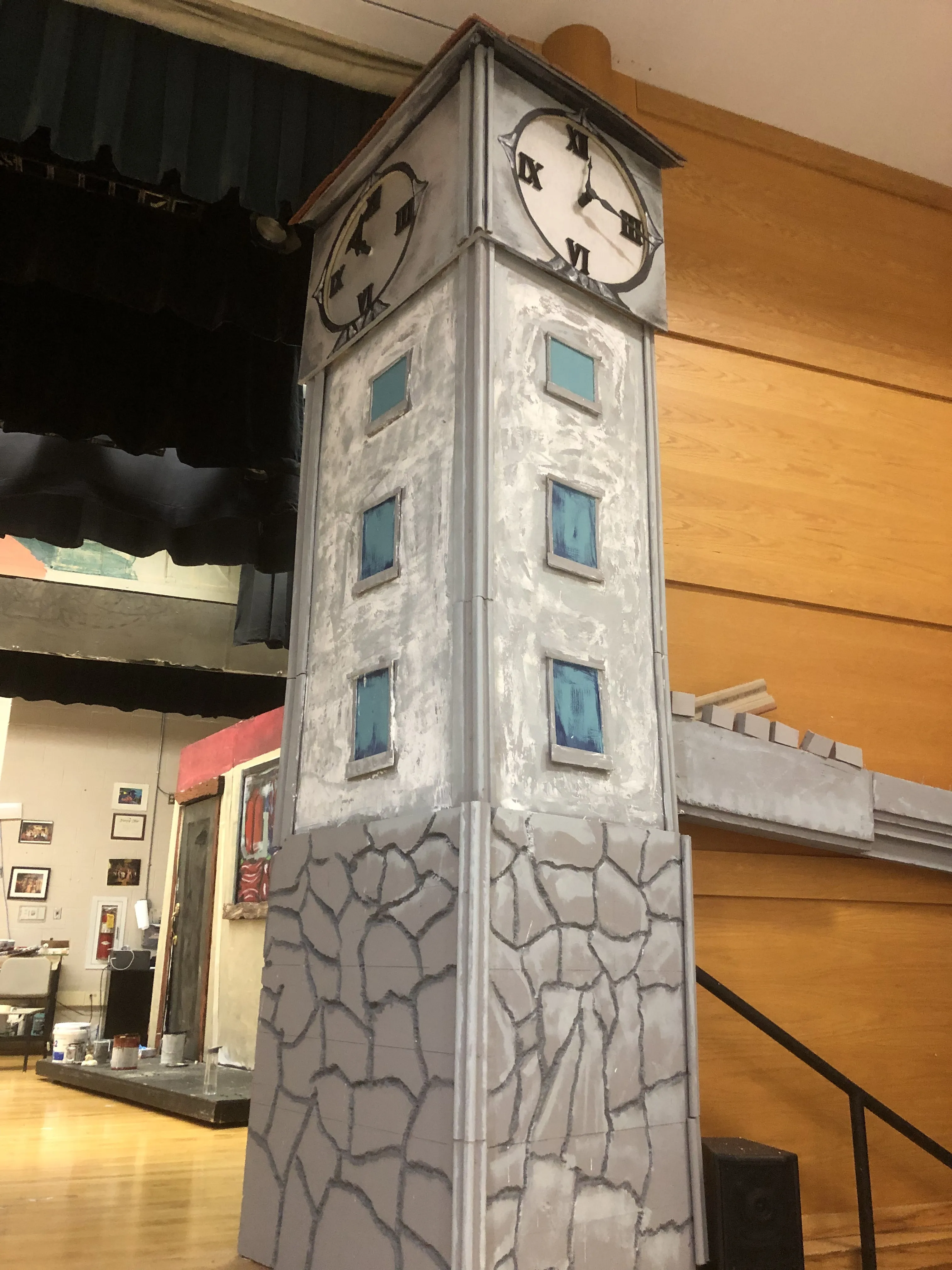 The complete tower assembled in daylight — stone base, blue windows, clock faces at top