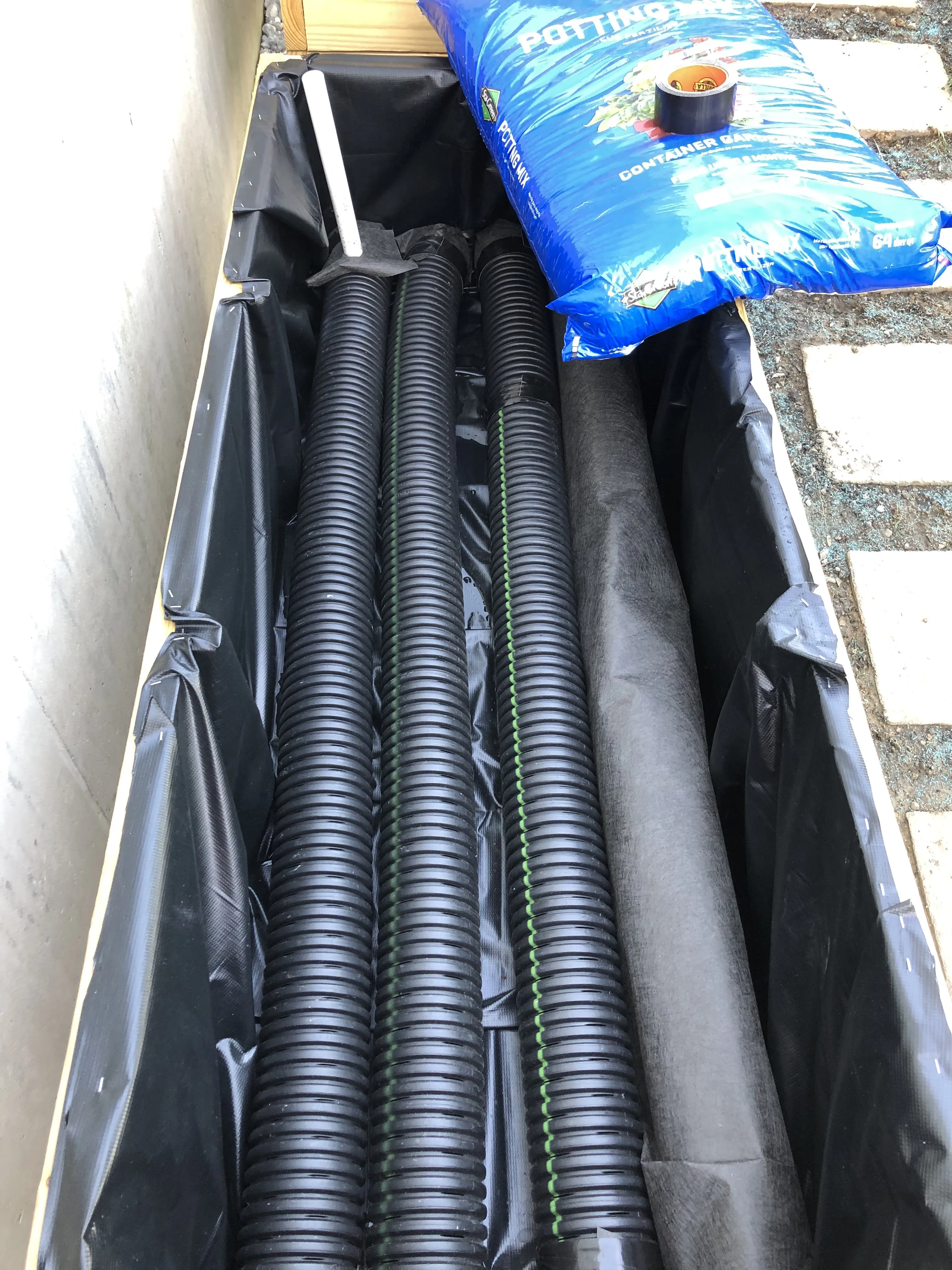 Inside the bed before filling — black liner, corrugated drainage pipes, landscape fabric