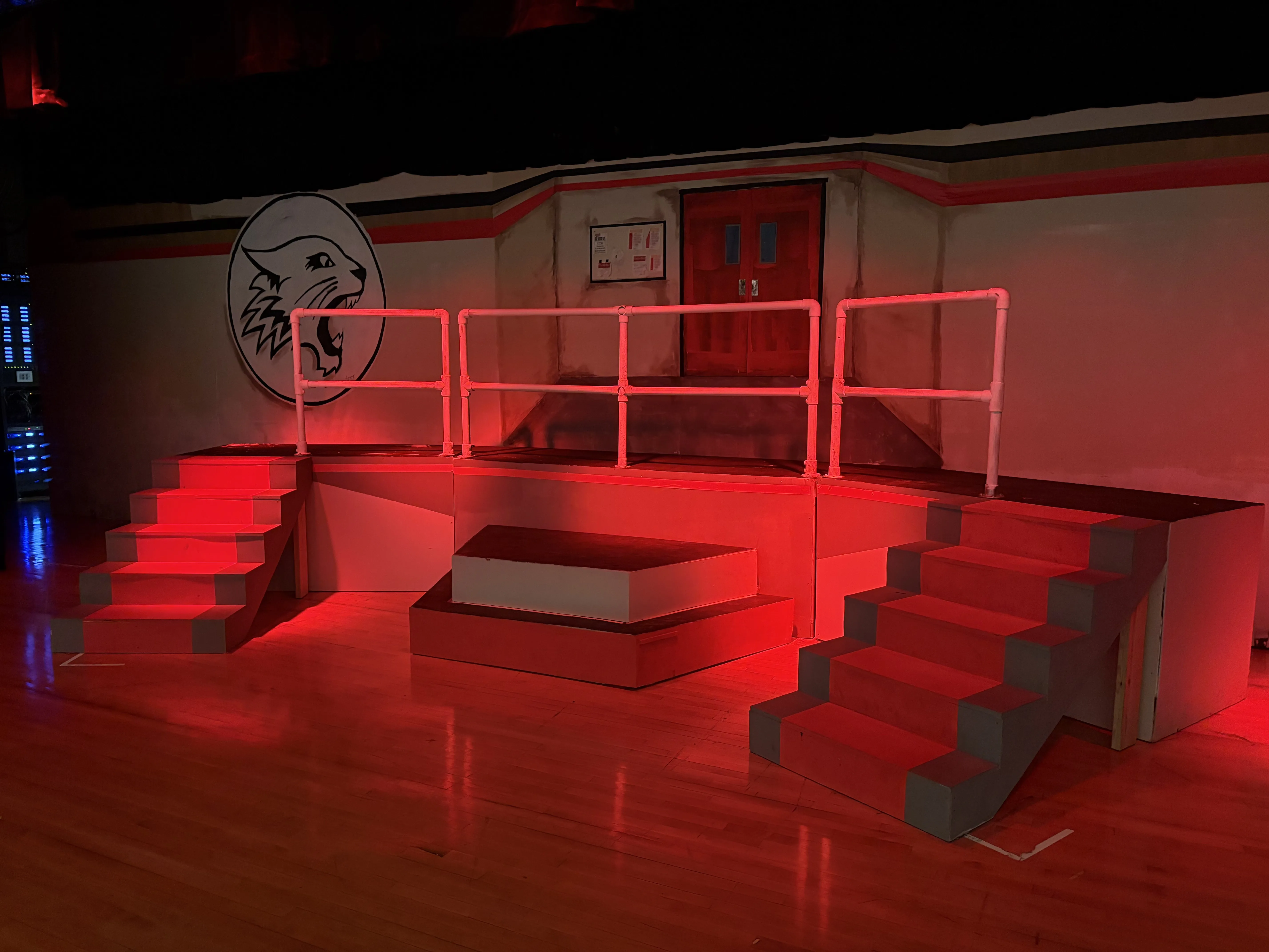 The finished set under red stage lighting — platforms, stairs, railings, and the Wildcat