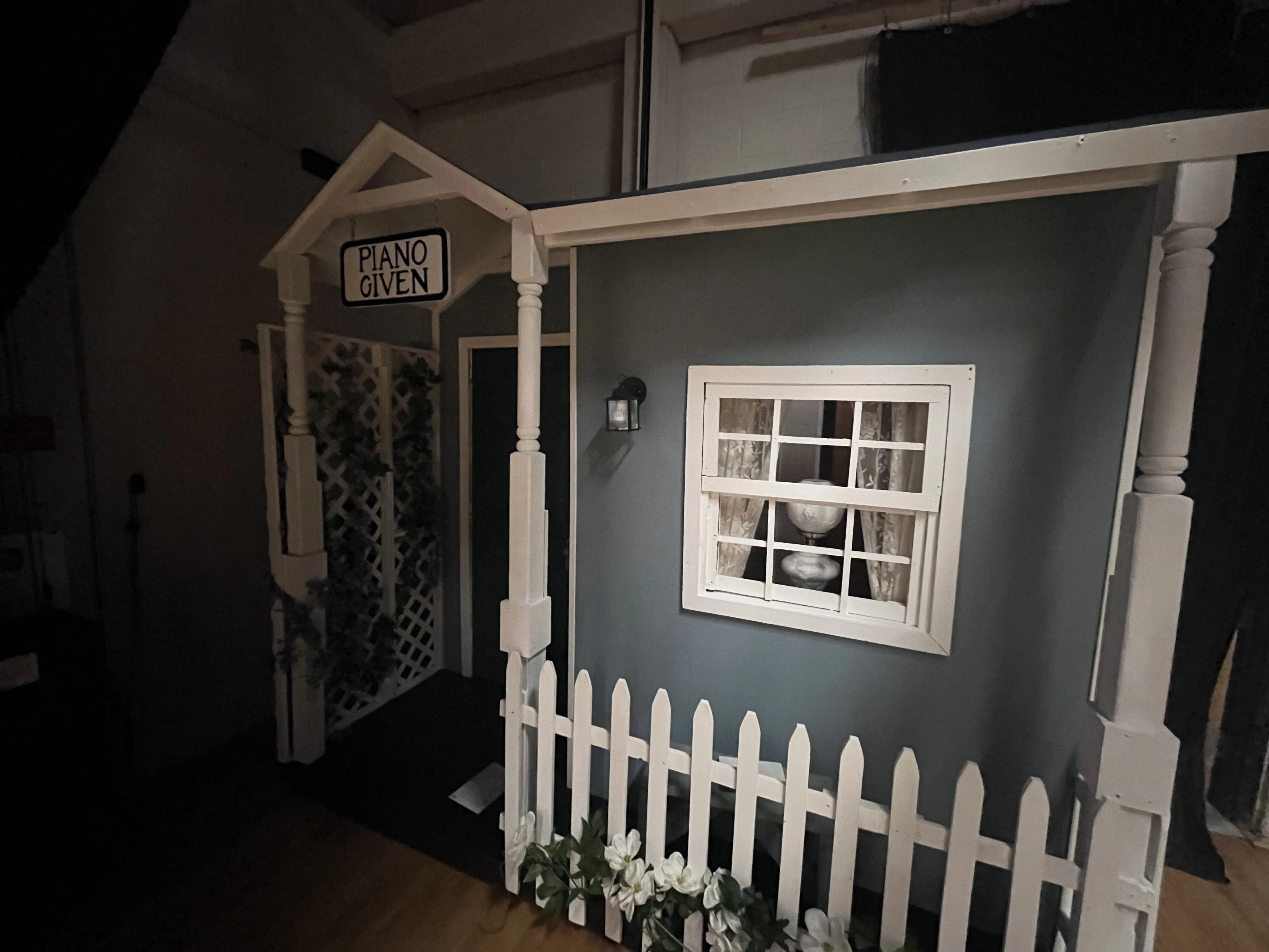 Marian's house exterior — blue-gray with white trim, "Piano Lessons Given" sign, teal door, white picket fence, lattice